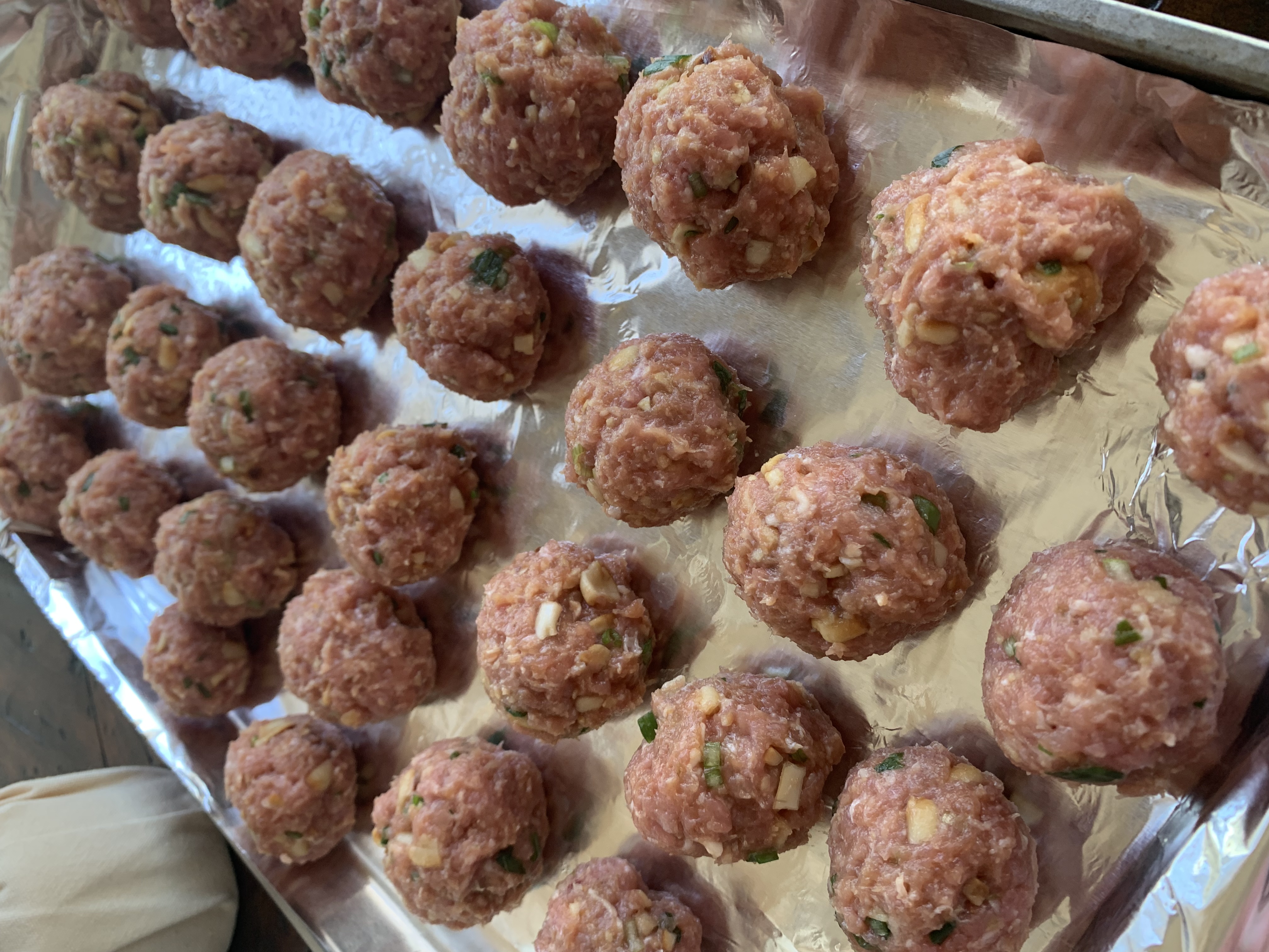 Raw meatballs on a cookie sheet that are sitting on top of foil to rest before cooking.