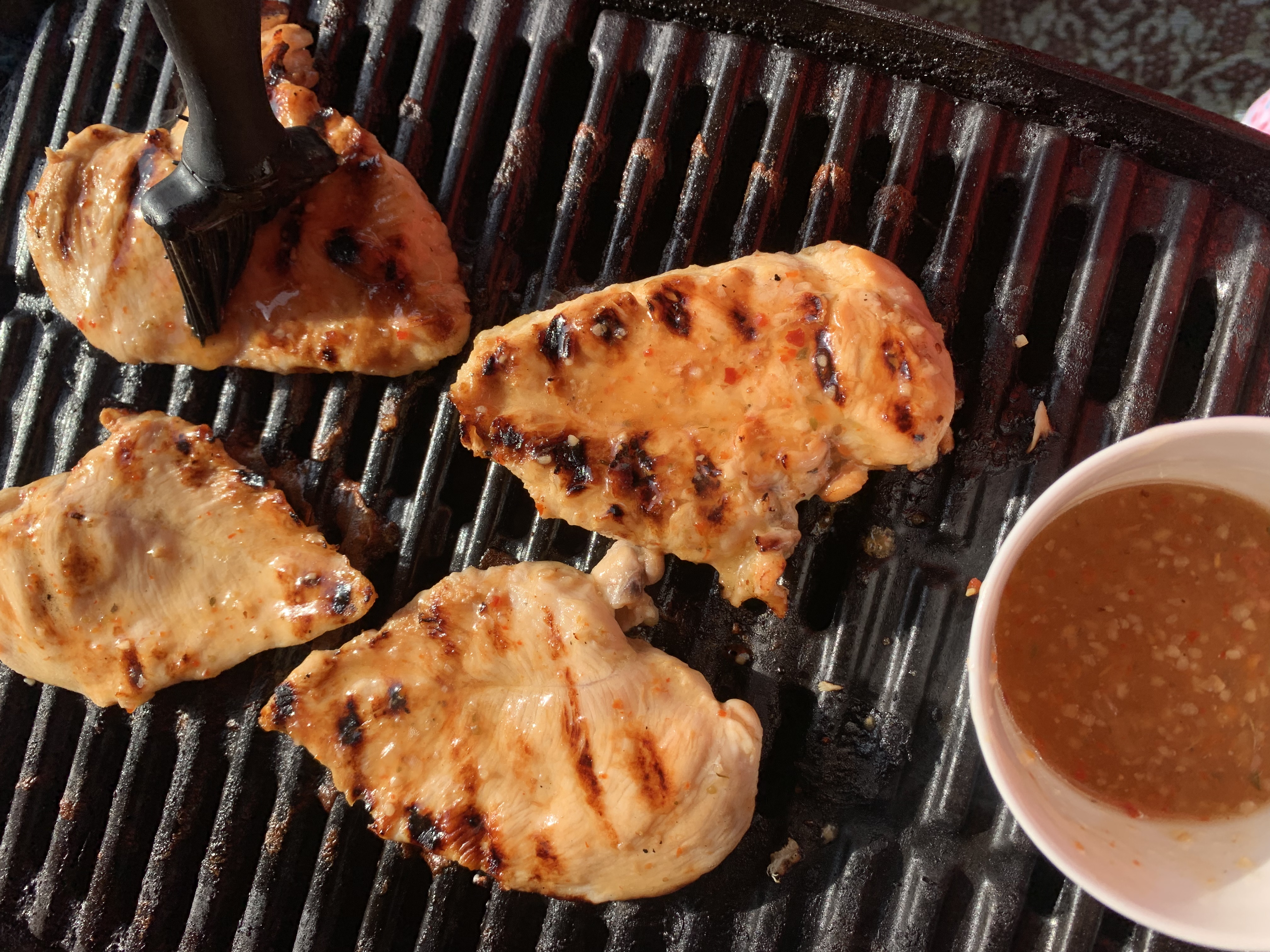 4 Chicken breasts on a weber grill being basted with Italian dressing.