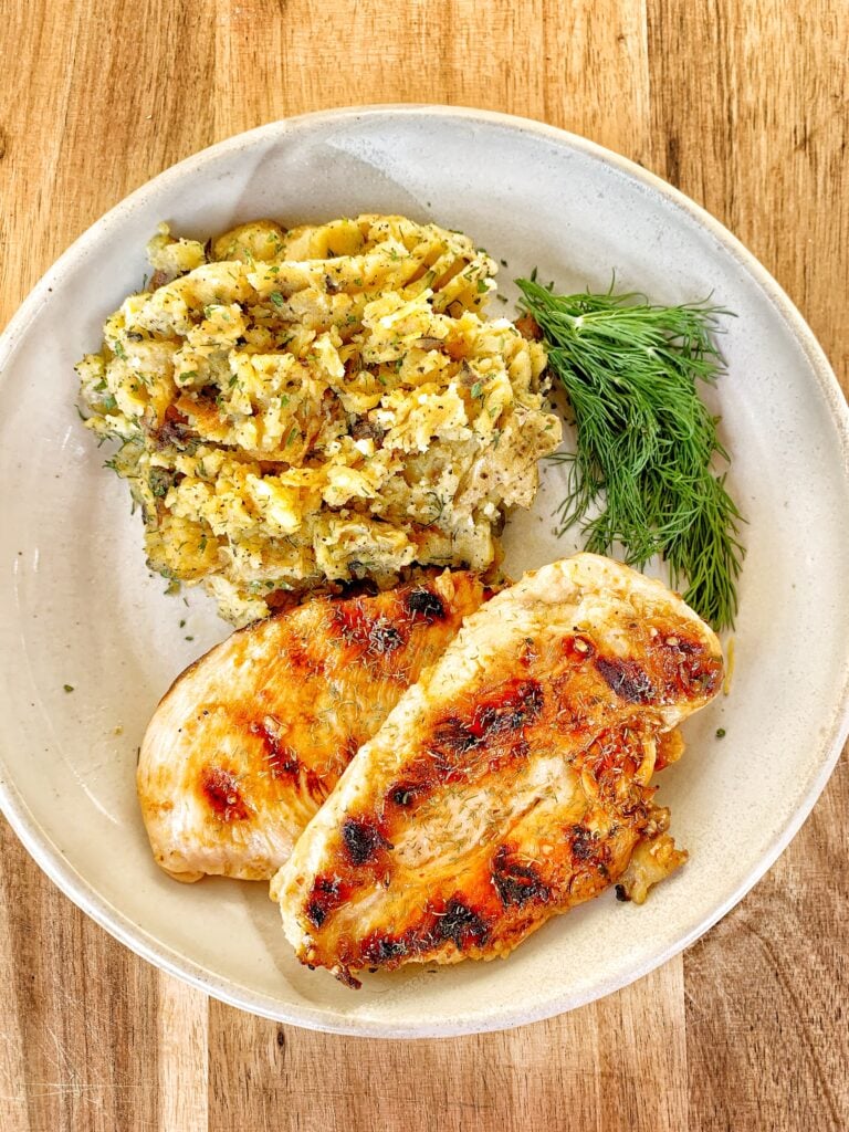 Two grilled chicken breasts, mashed potatoes and a sprig of dill
