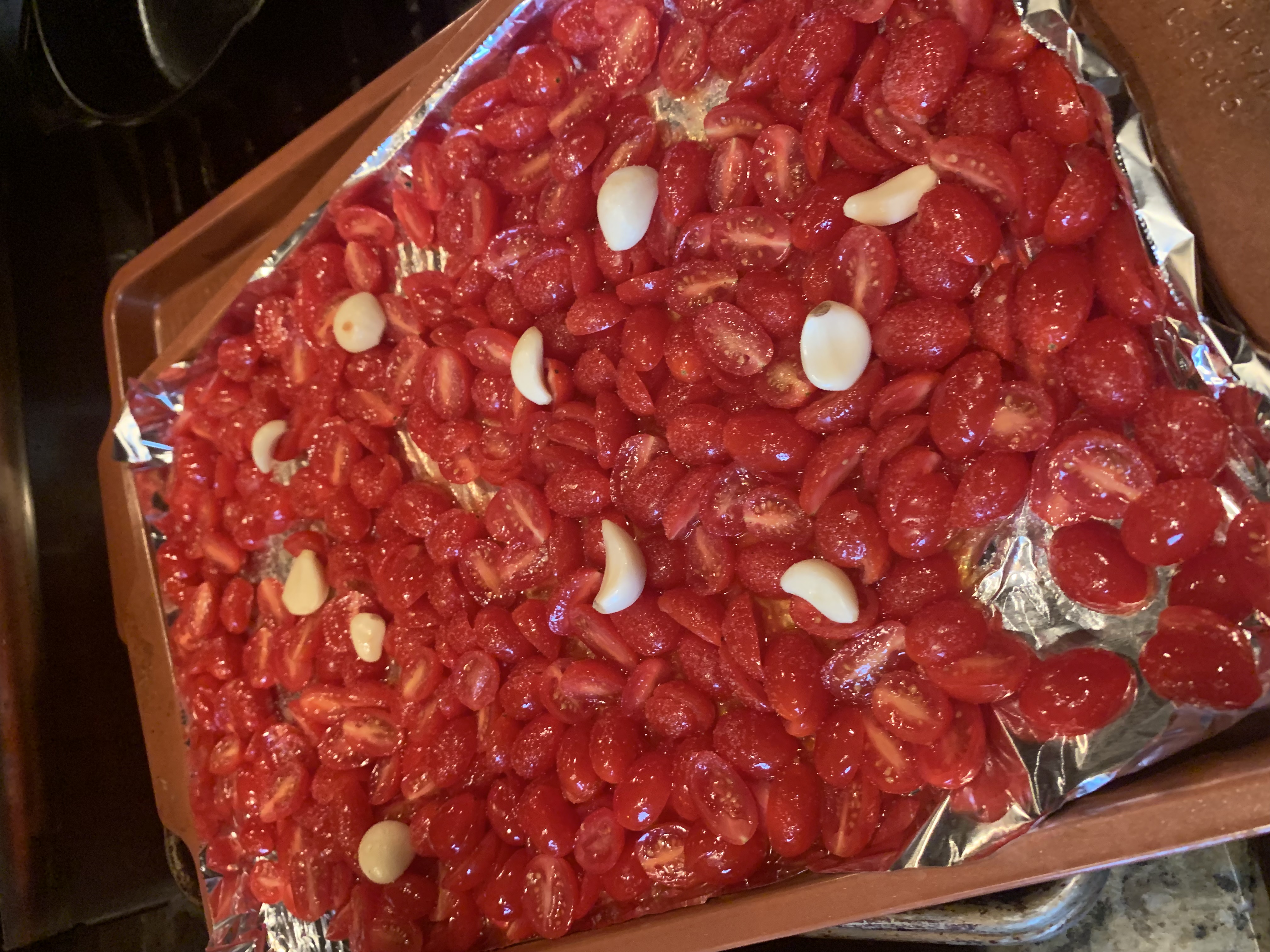 A sheet pan with salted tomatoes and garlic in olive oil on it.