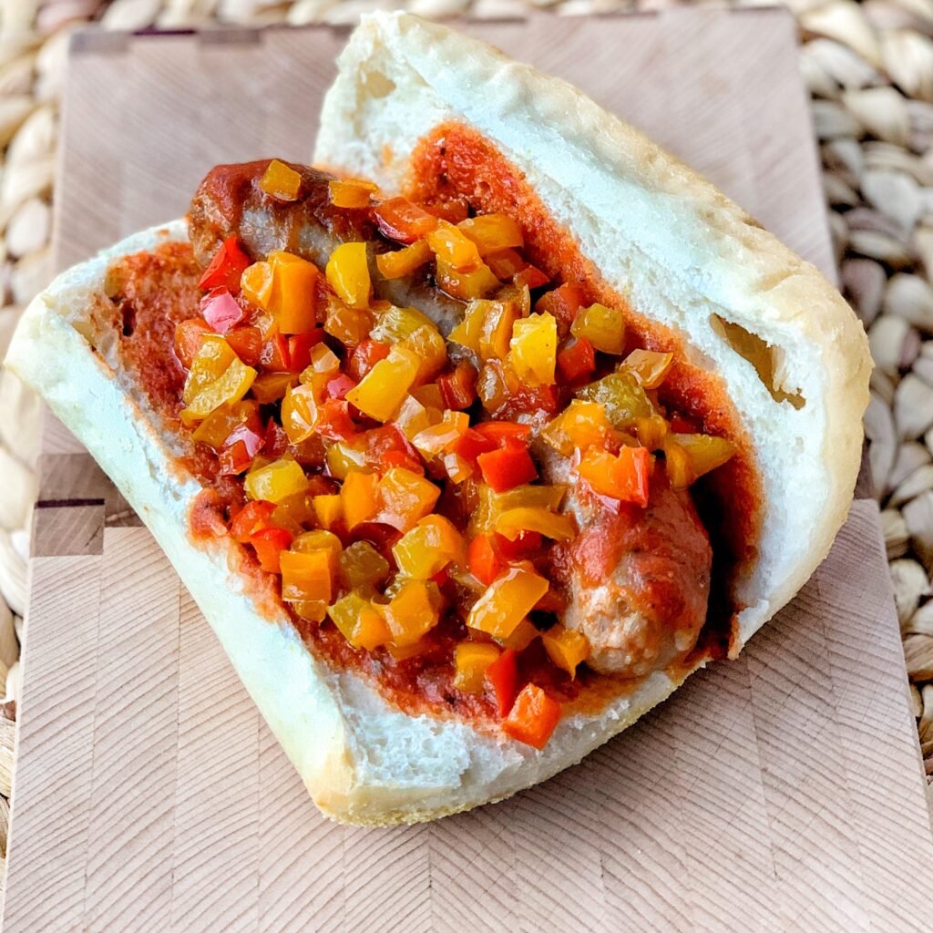 An Italian sausage in a bun topped with chopped peppers