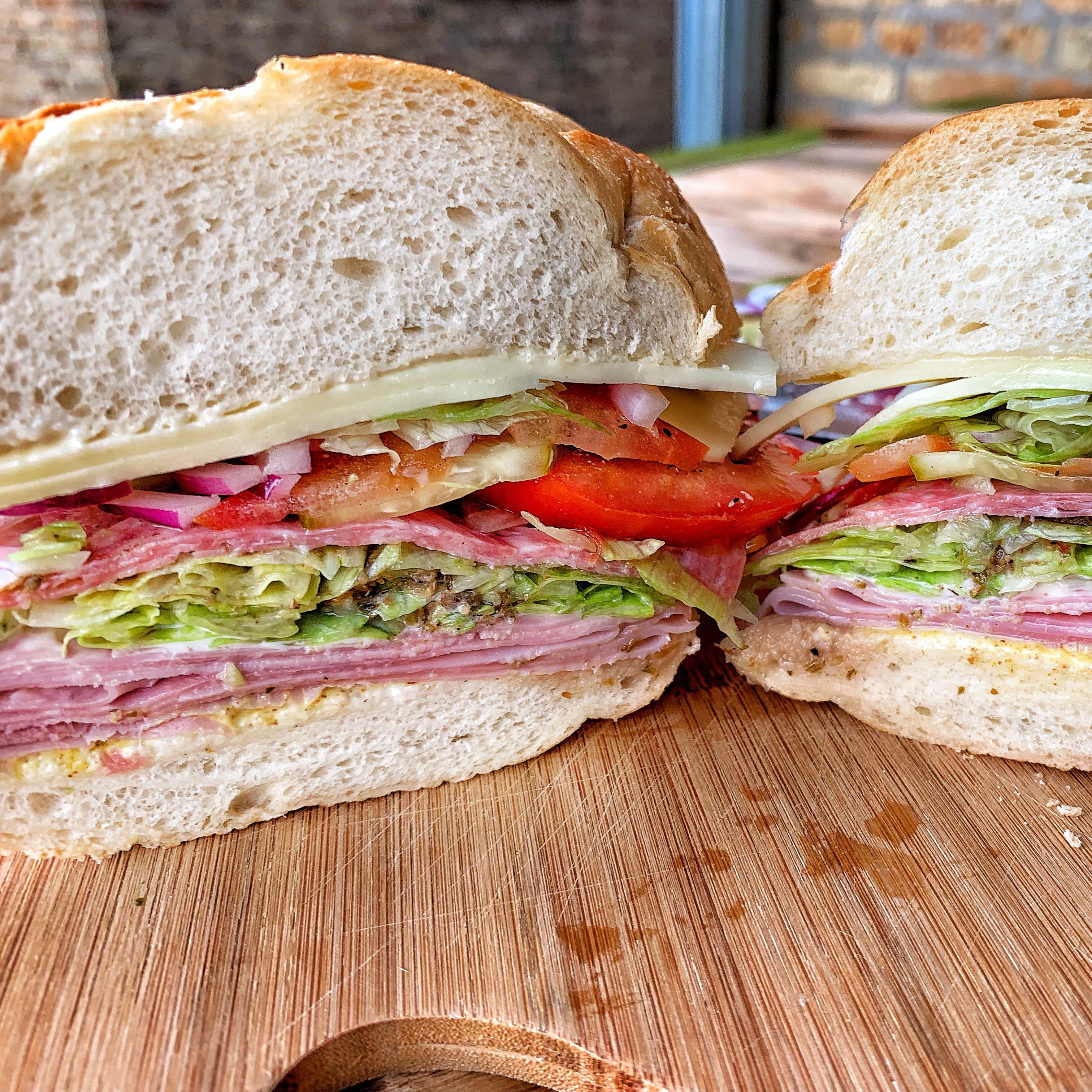 Picture of a sandwich cut in half showing all the layers of deli meat, cheese and veggies.
