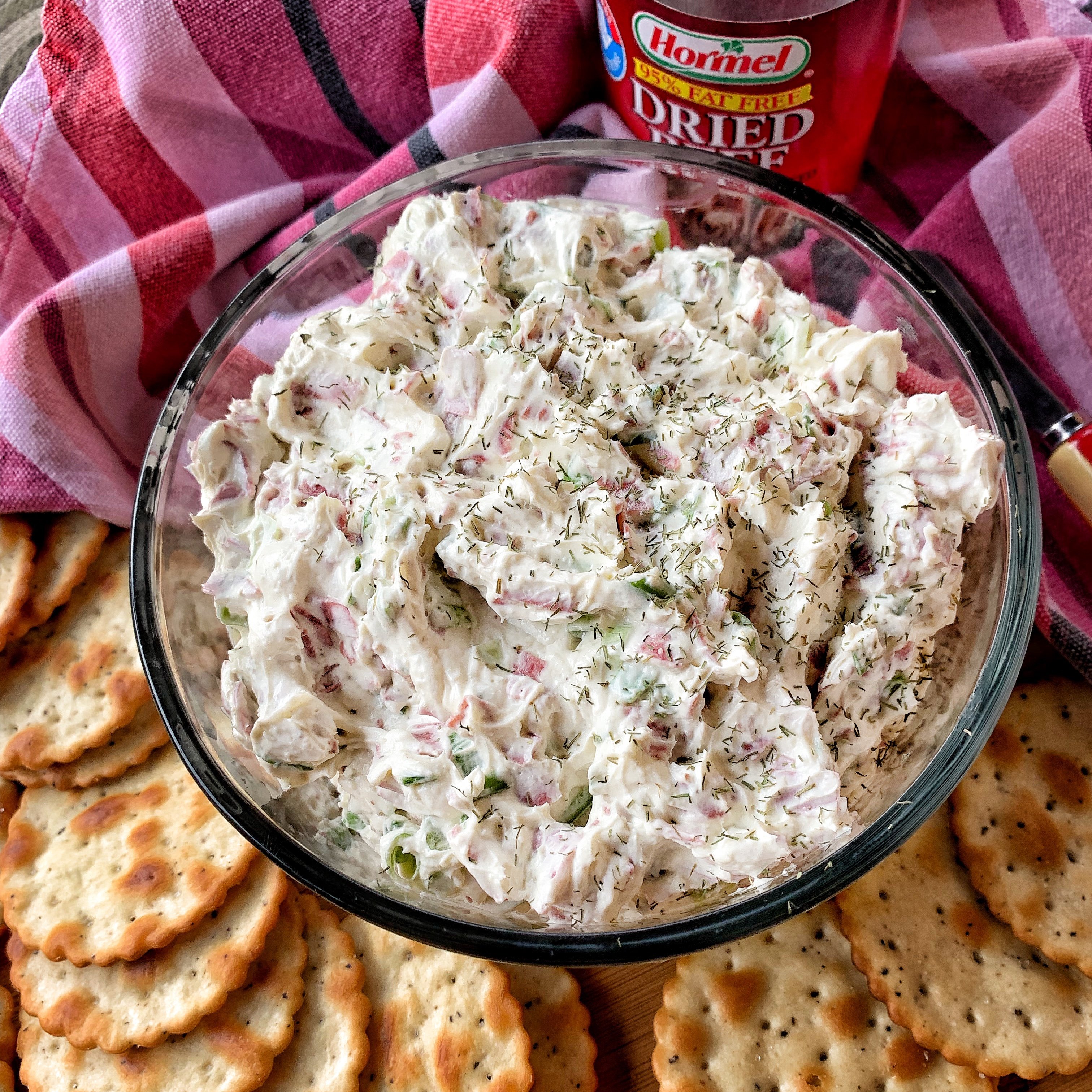 Bowl of party dip surrounded by crackers and the jar of hormel dried beef. 