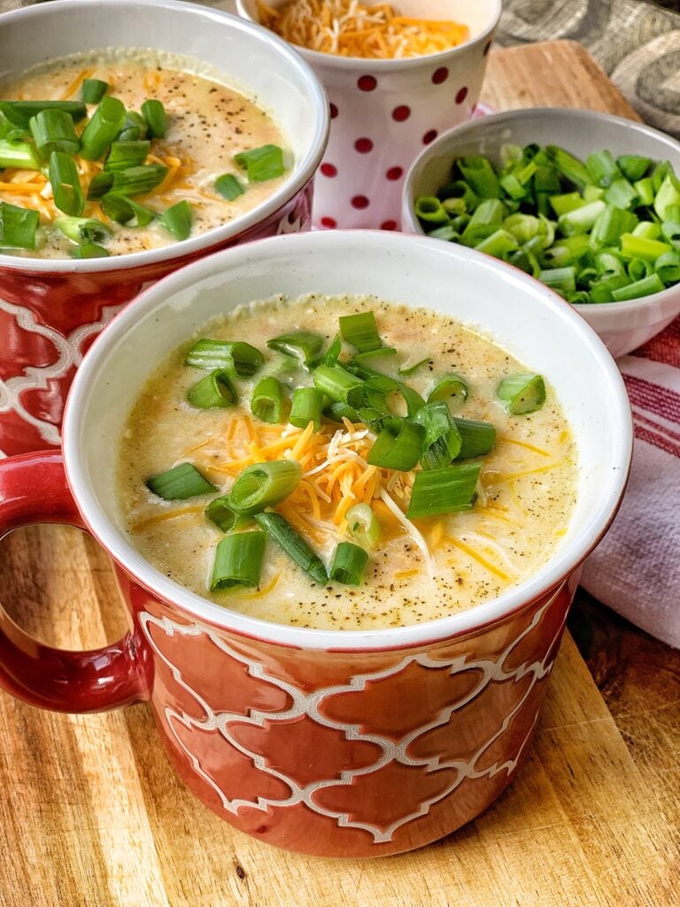 Two mugs of potato soup with cheddar cheese and green onions.