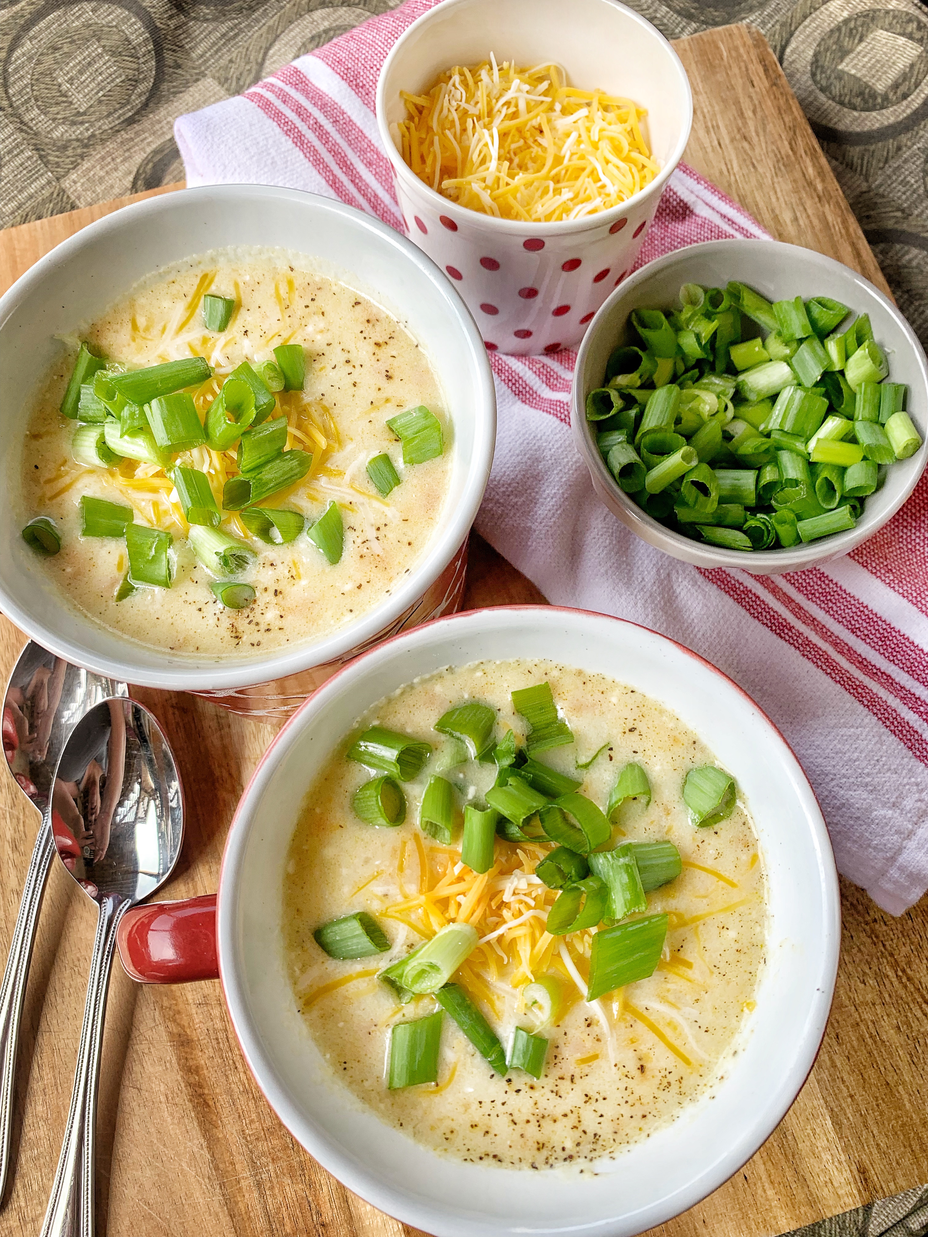 Two mugs of potato soup with green onions and cheese seen from above