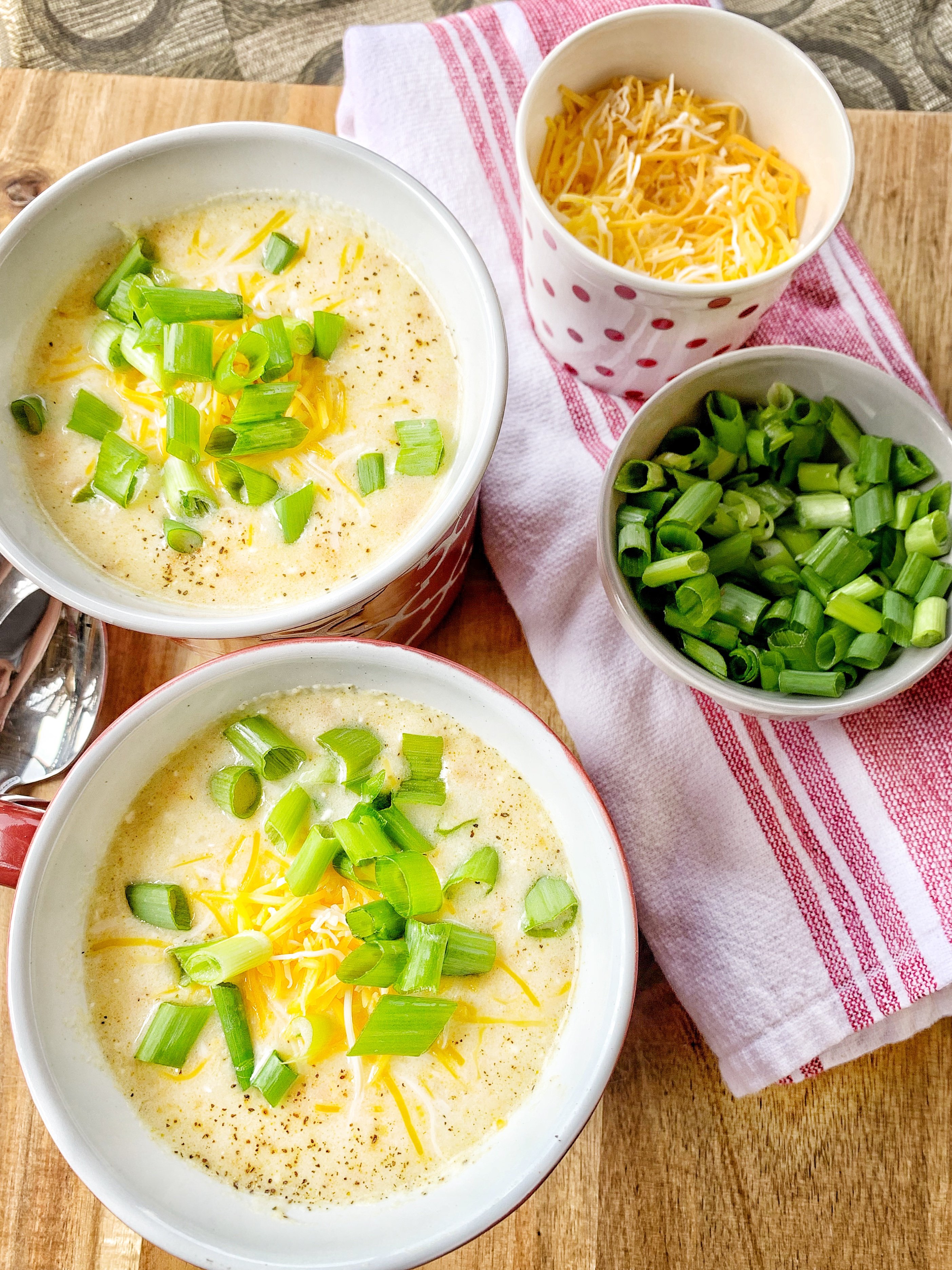 Two mugs of soup with green onion and shredded cheese