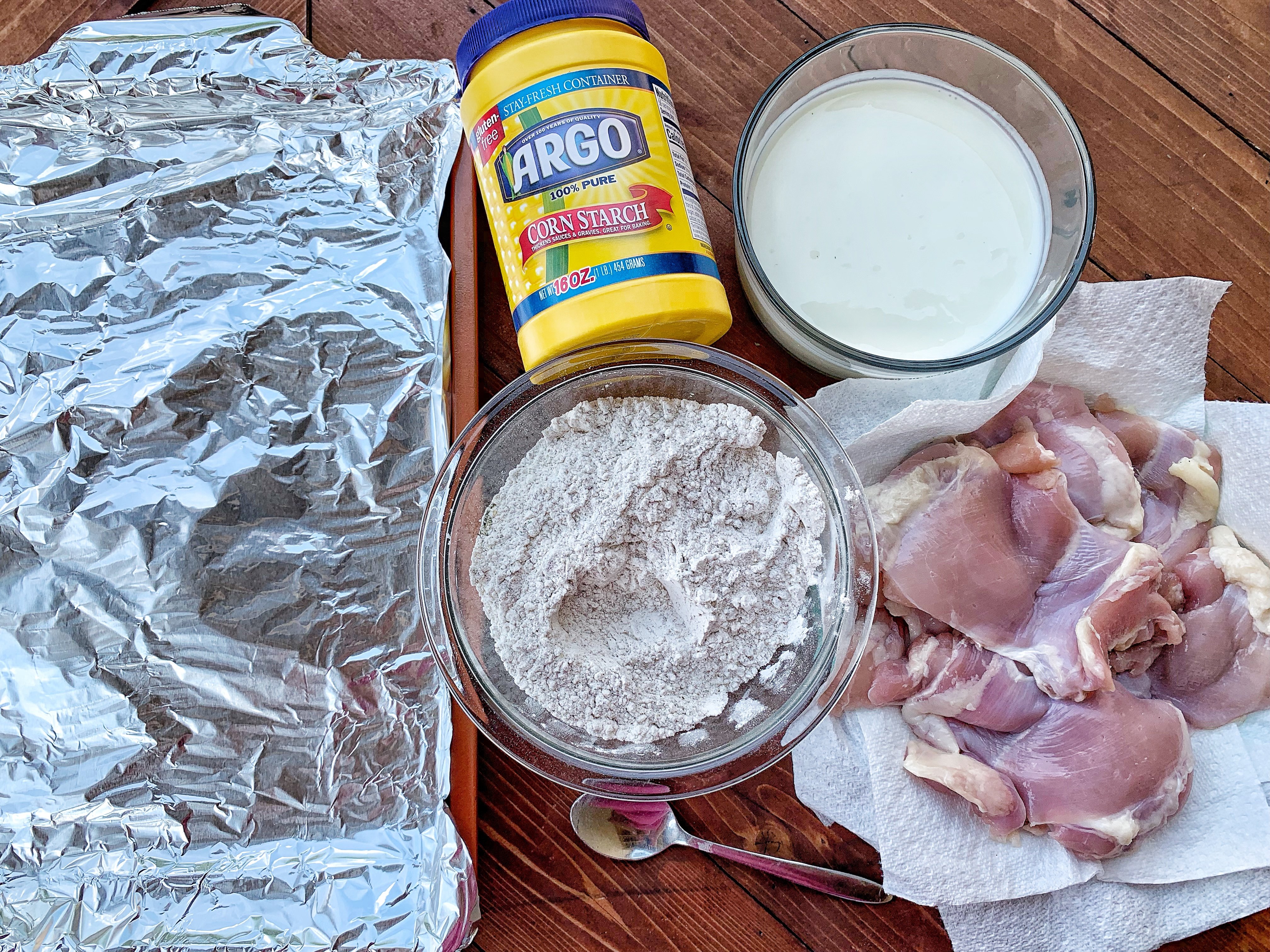 The breading station for making fried chicken, including raw chicken, corn starch, and Greek yogurt