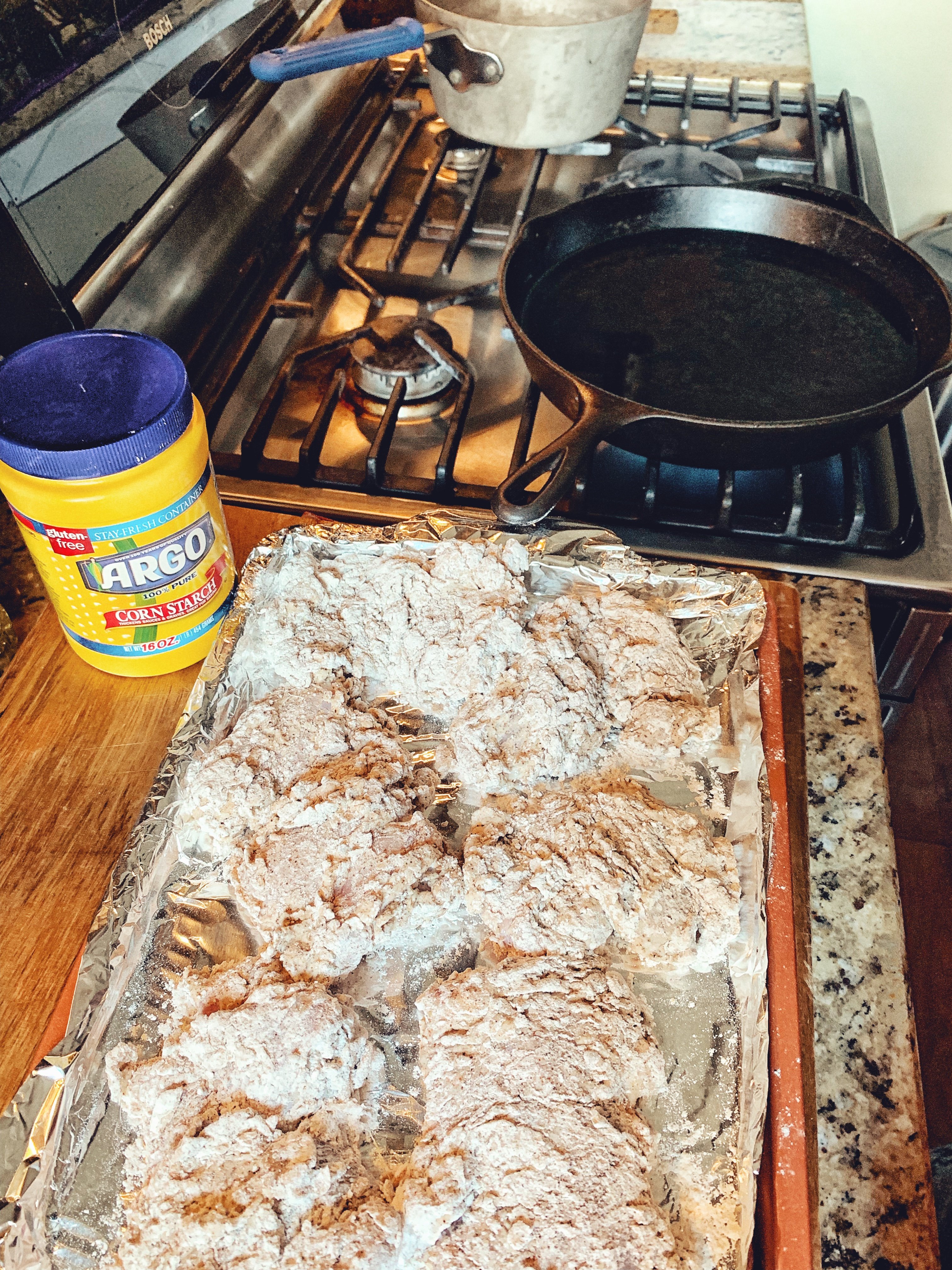 The frying station, including a skillet on the stove and breaded chicken 