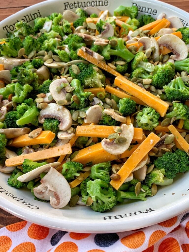 A white bowl with bright green broccoli, cheddar cheese slices and mushrooms