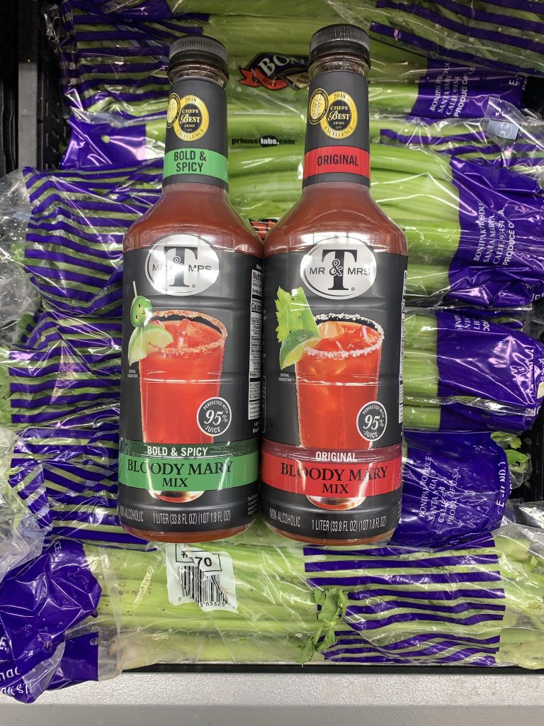 Two bottles of Bloody Mary mix on top of of packages of celery