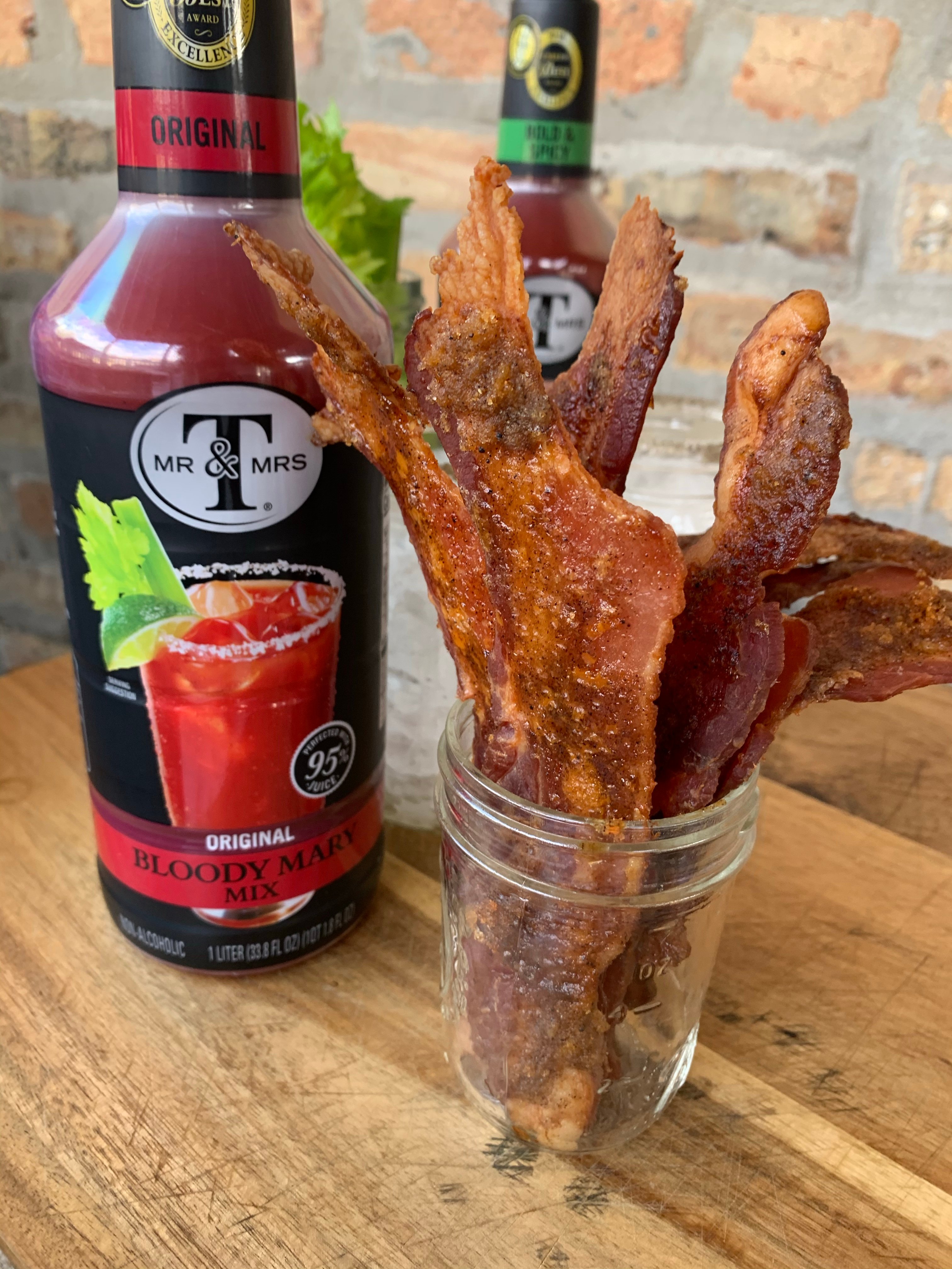 A bottle of Bloody Mary mix next to a cup of bacon