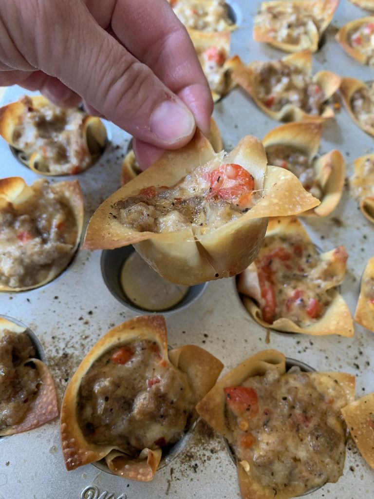 A crumbled sausage and creamy cheese wonton held above other wontons still in the muffin tin