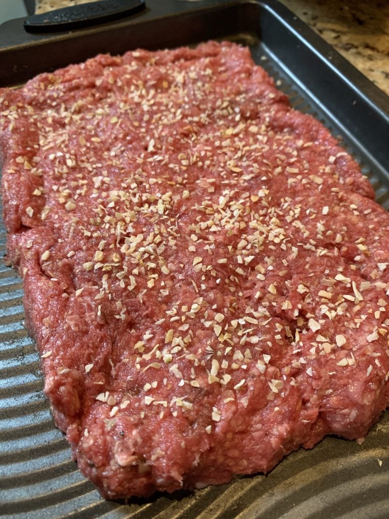 Ground meat formed into a large beef patty with onion flakes on top