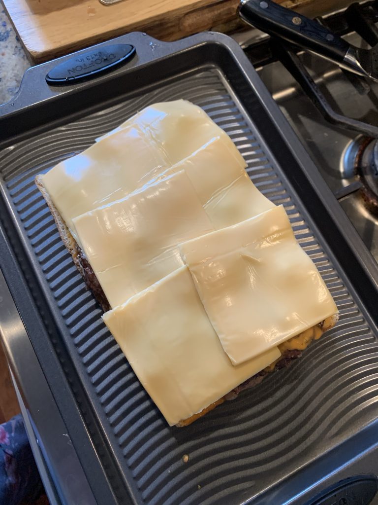 Slices of Kraft American cheese on ground meat formed into a large beef patty