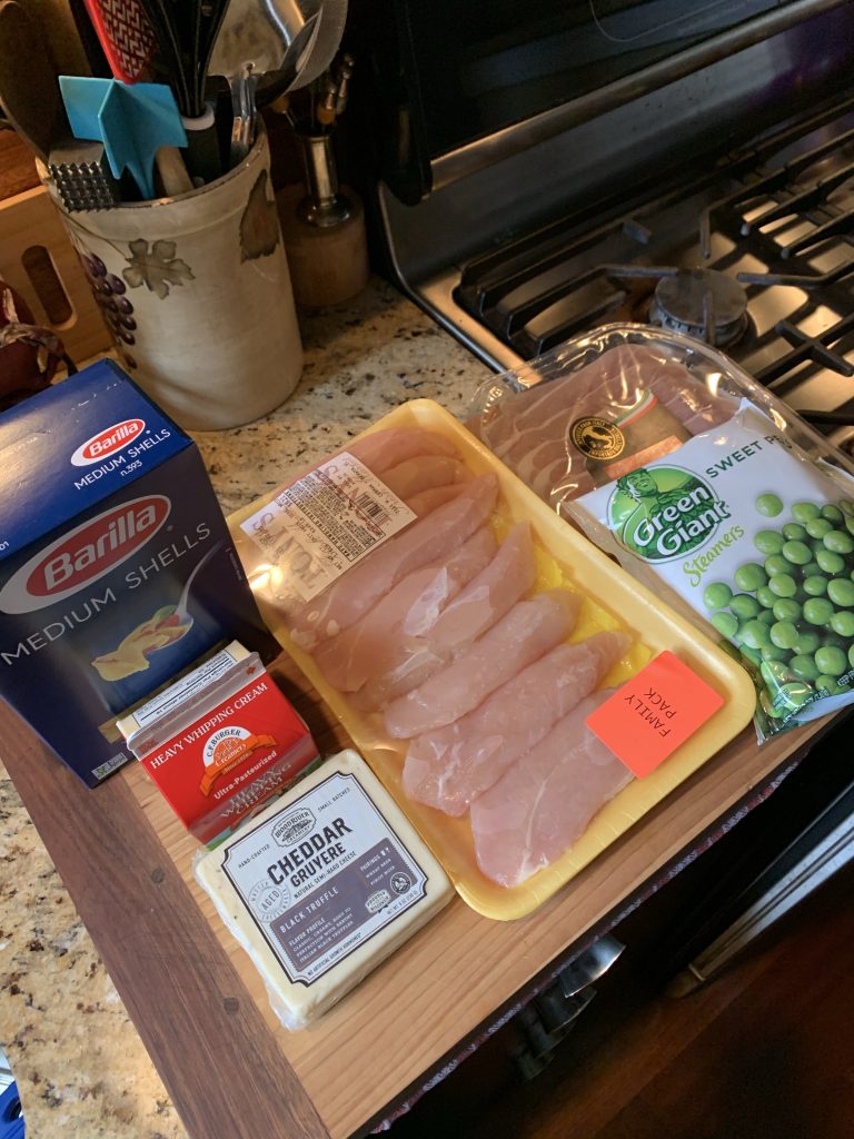 The ingredients for the dish including chicken, pasta shells, cheddar, heavy whipping cream, green peas, and prosciutto 