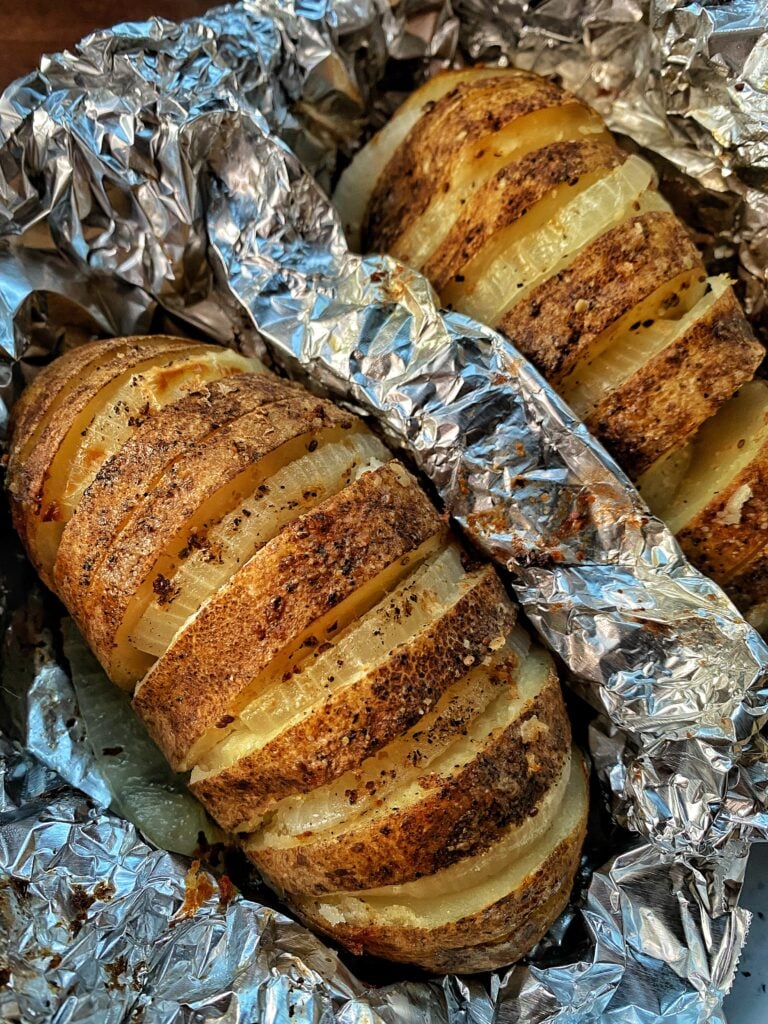 Two Idaho Russet Potatoes with onions, salt, pepper, herbs and spices and delicious melted butter sliced with onions in the slices