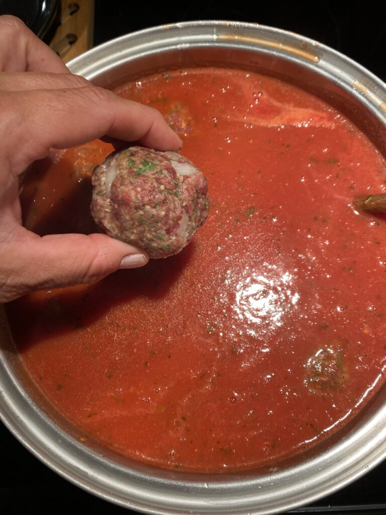 A raw meatball about to be dropped into a pot of red sauce