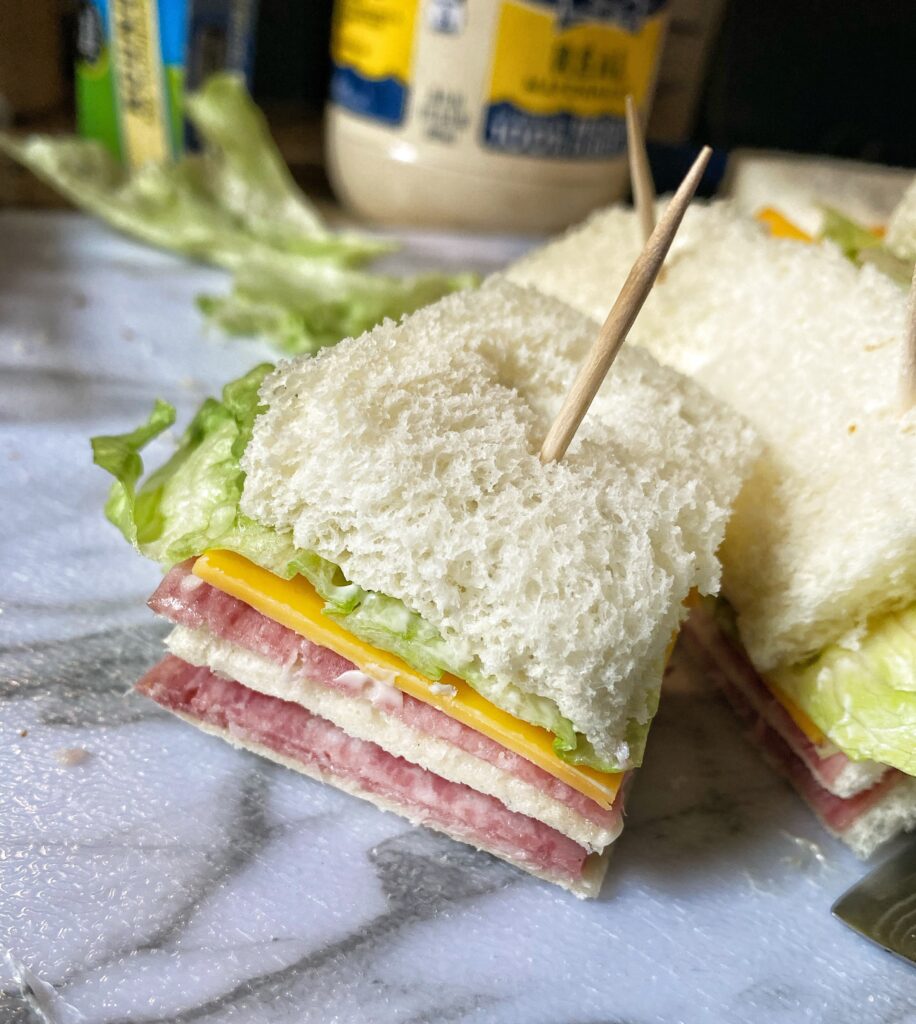 A close up of a small meat and cheddar sandwich with a toothpick