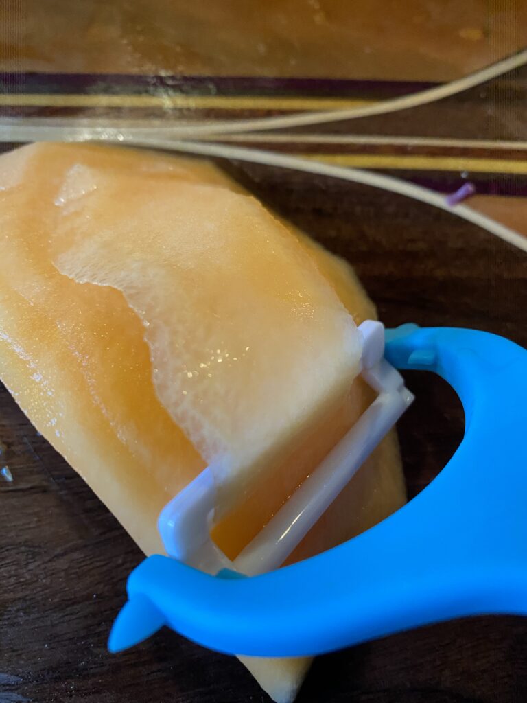 A slice being peeled off of a canteloupe 