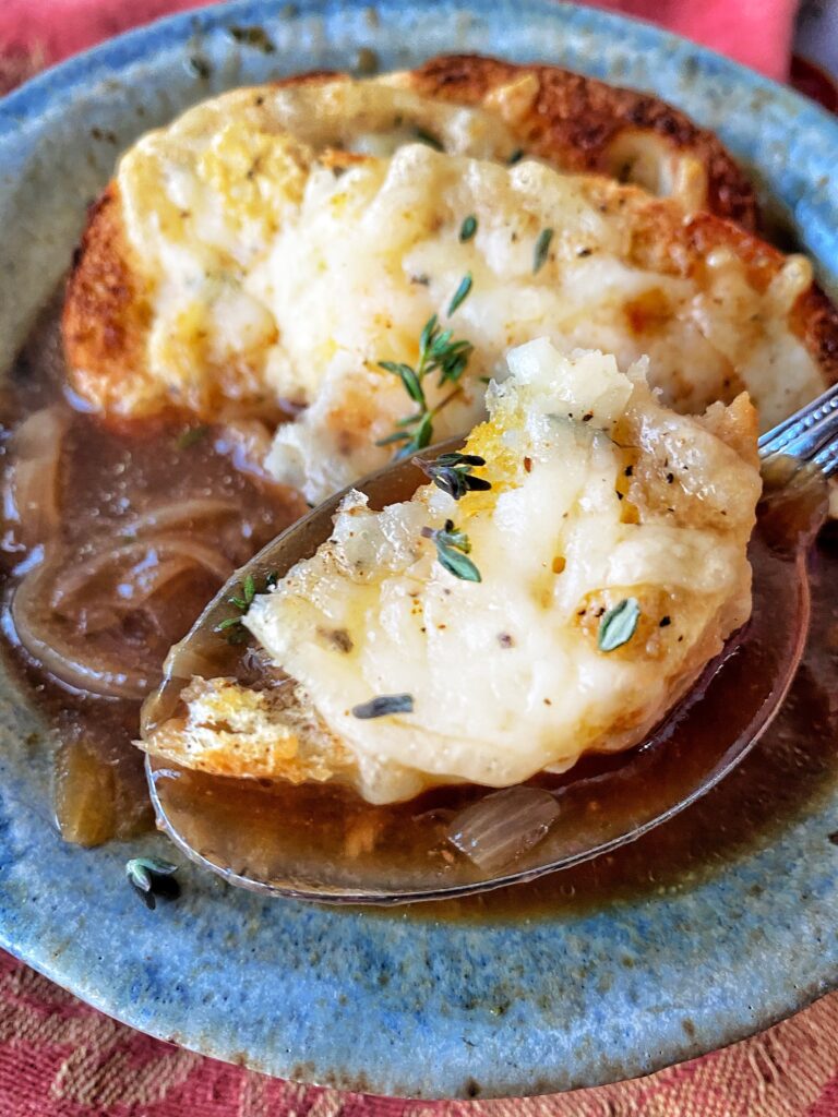A spoon with French Onion Soup and a cheesy bread dumpling on top