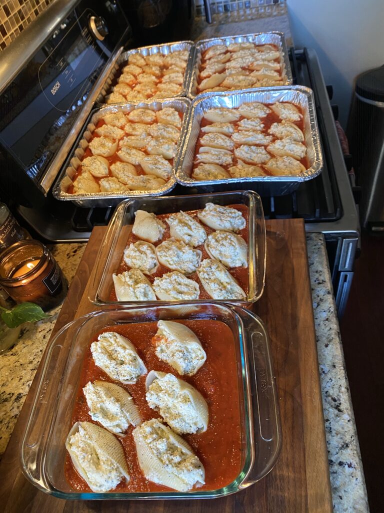 Four tins of stuffed shells in sauce on top of the stove with another two glass dishes of the same on the counter