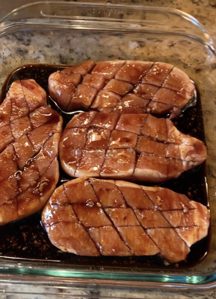 Scored pork chops marinating in a glass baking dish