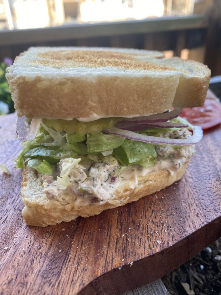 A tuna salad sandwich with onions, pickles, and lettuce