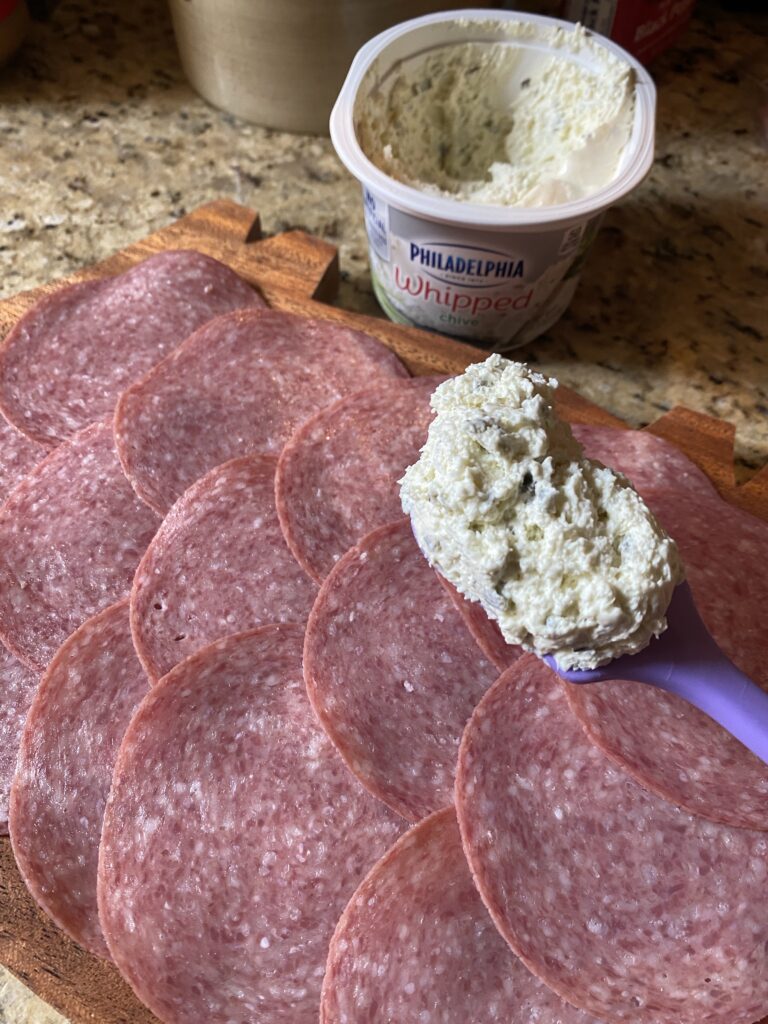 Cream cheese about to be spread on  the slices of salami