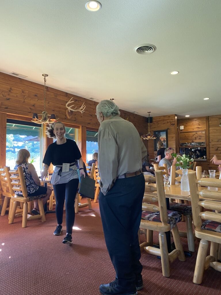 The inside of the Chef Rene restaurant with customers eating at their tables, a waitress, and Chef Rene's dad 