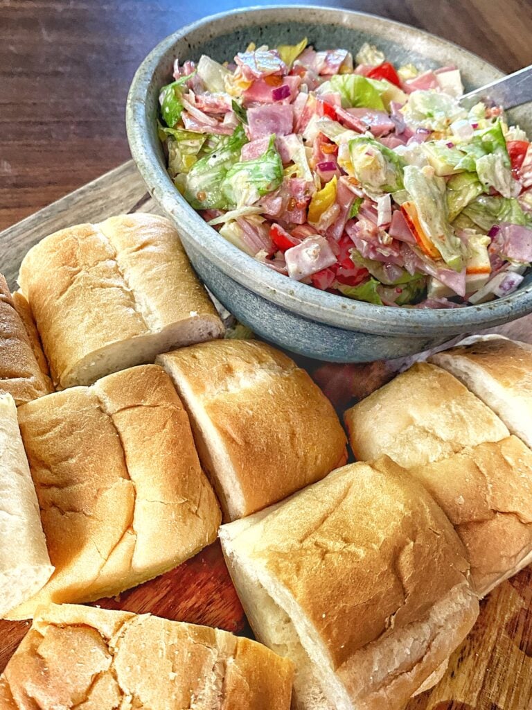 Italian chopped sandwich mix in a bowl surrounded by chopped sub rolls