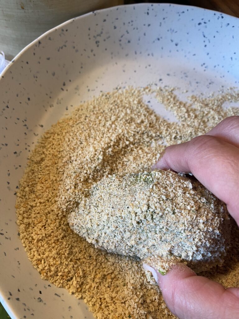 An avocado half being coated in breading mix
