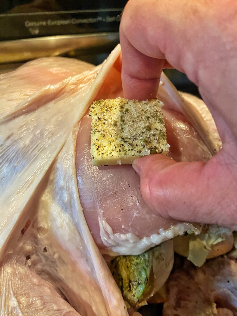 A seasoned butter pat being placed under the skin of a raw turkey