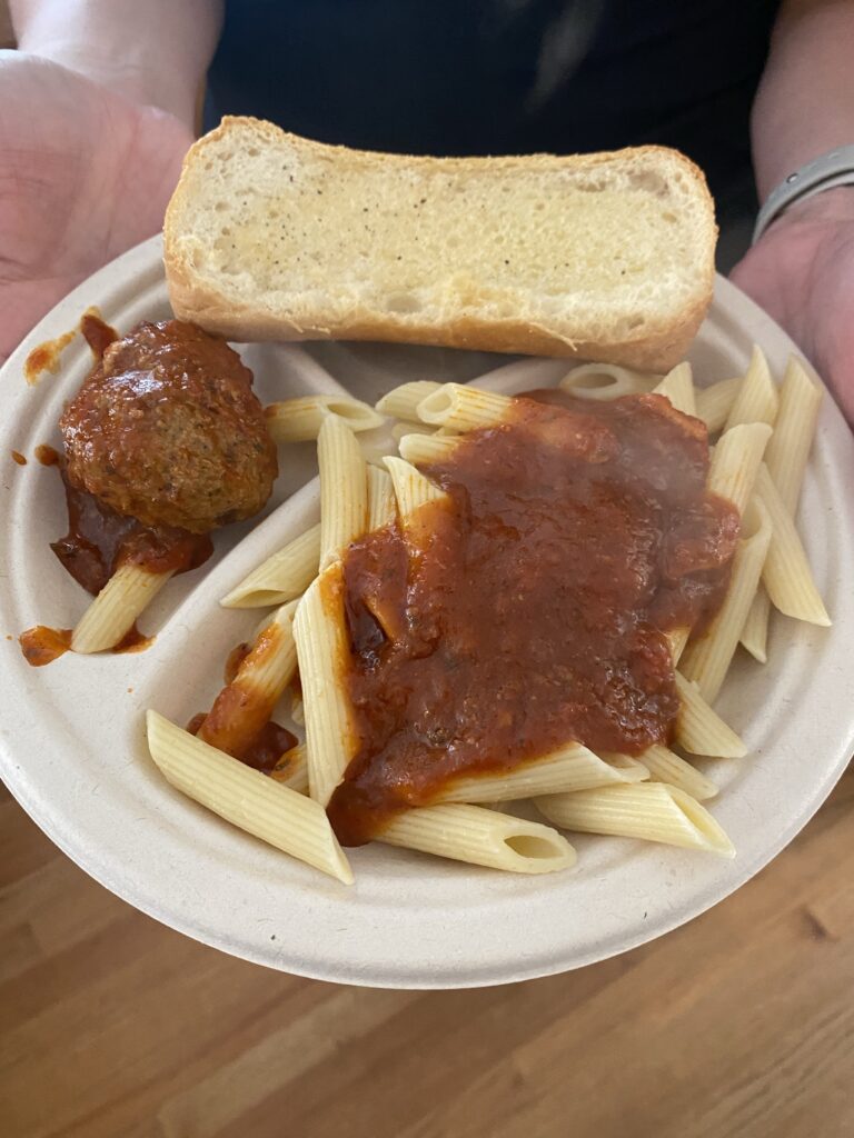 A plate with garlic bread and pasta and a meatball both topped with Sunday sauce