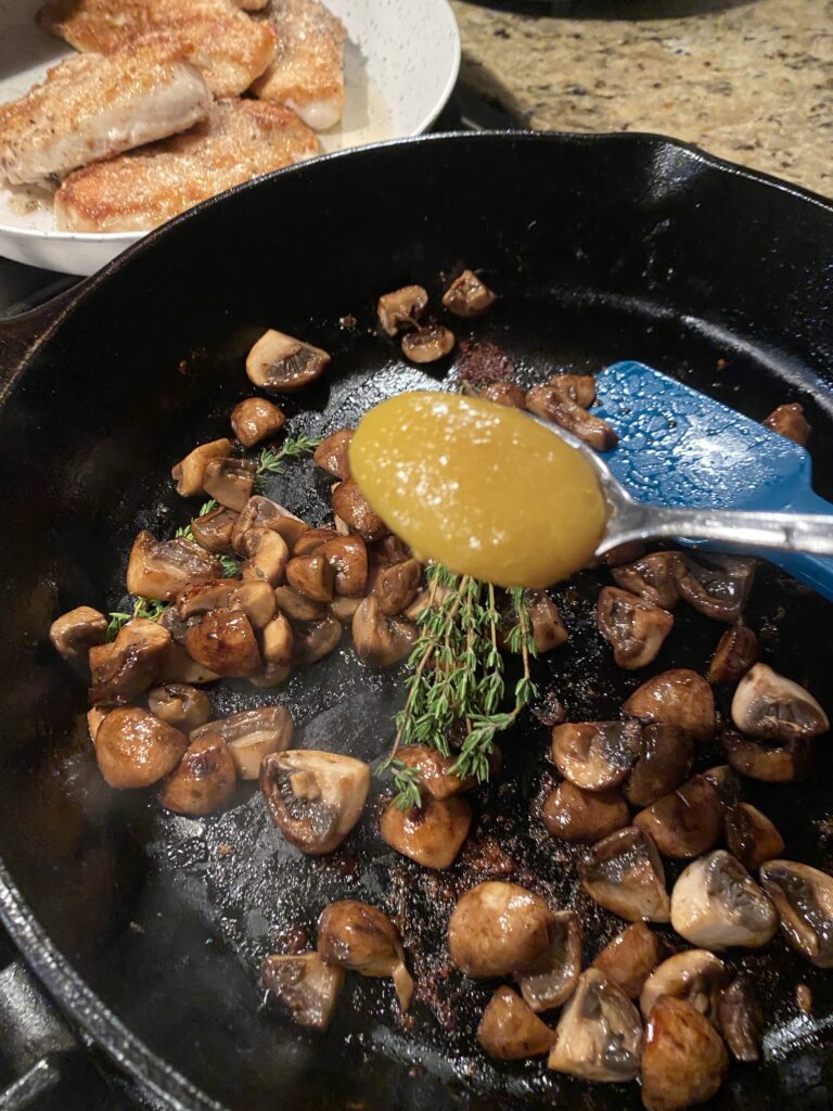 Mushrooms and thyme in a skillet with a spoon of sauce over it
