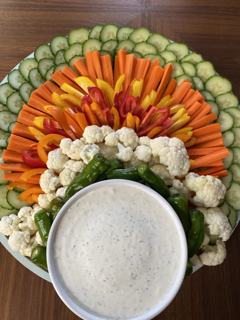 A white bowl of ranch dressing surrounded by various veggies arranged into the body of a turkey