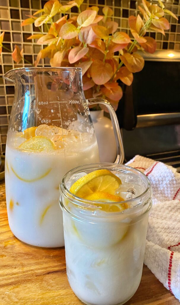 A glass pitcher of creamy lemonade with fresh lemon slices.
