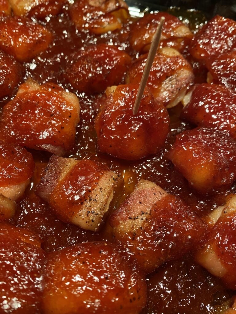 A bacon wrapped water chestnut with BBQ sauce on a toothpick among other bacon wrapped chestnuts