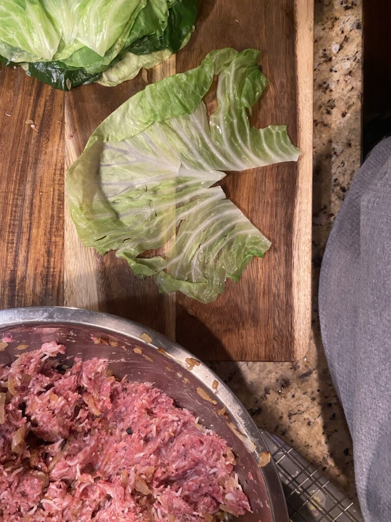 A cabbage leaf on a cutting board next to a bowl of meat mixture
