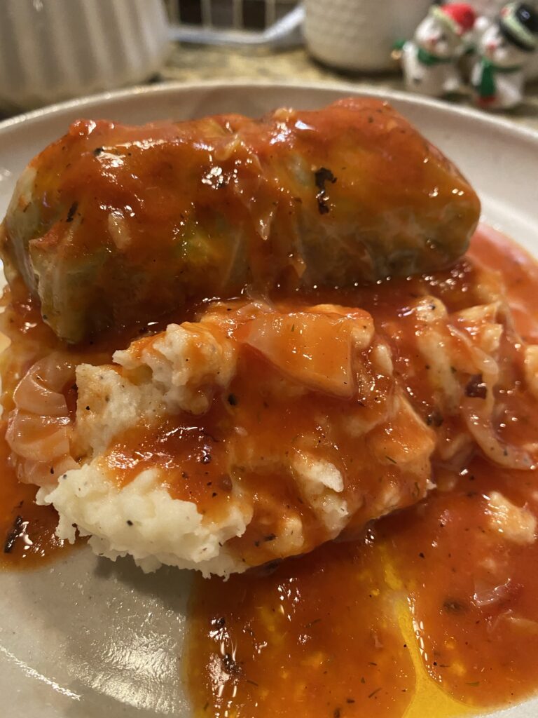 A finished stuffed cabbage over mashed potatoes topped with tomato sauce