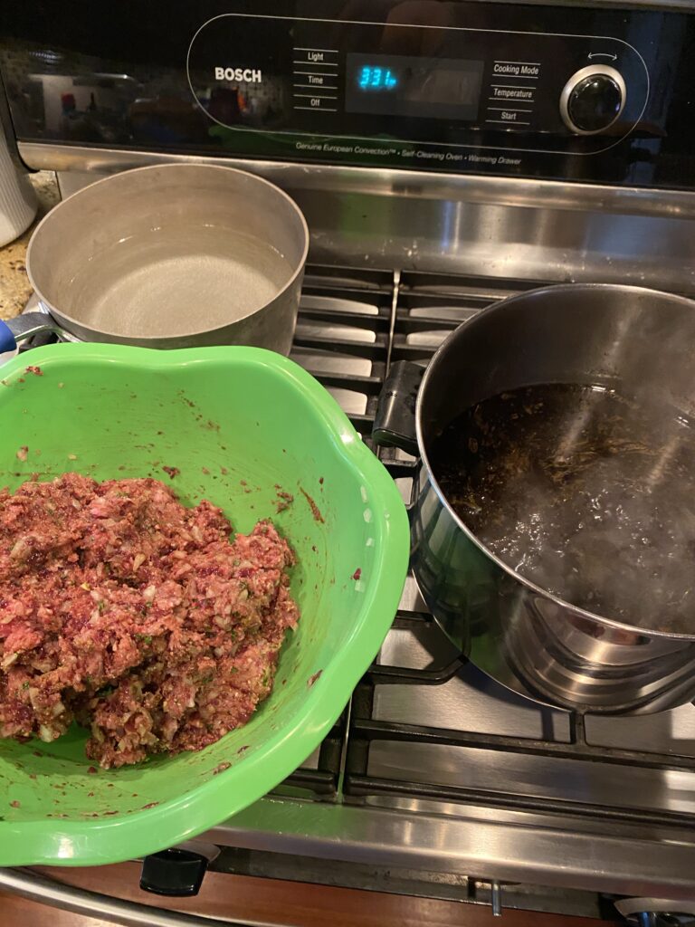 A green bowl of dumpling mixture next to a bubbling pot