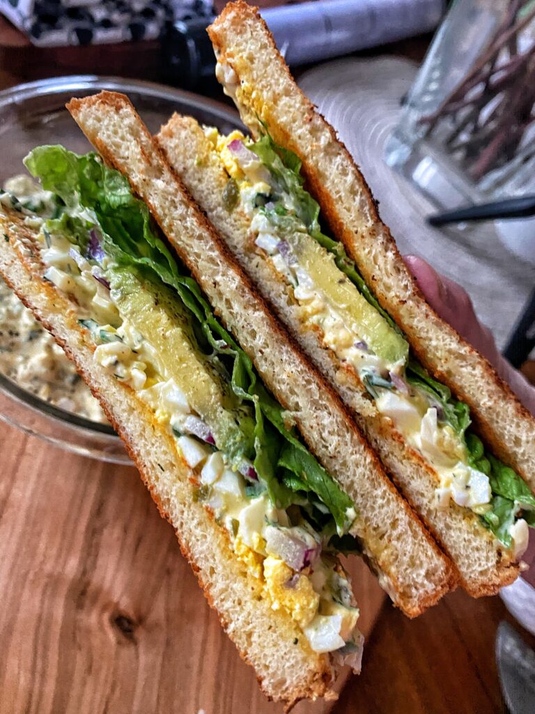 The finished egg salad sandwich being held up 