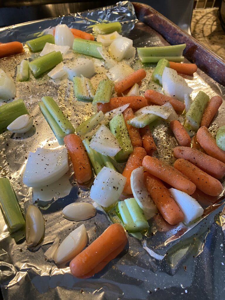 Carrots, celery, and onion with seasoning on a baking sheet