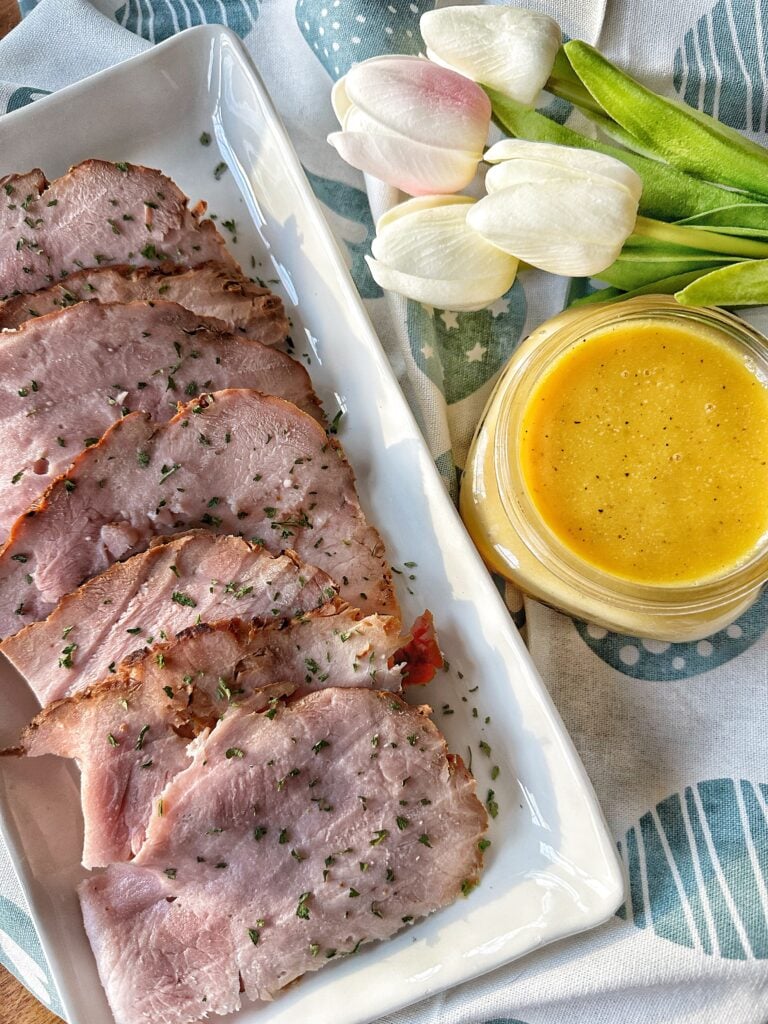 Slices of ham next to tangy yellow ham sauce