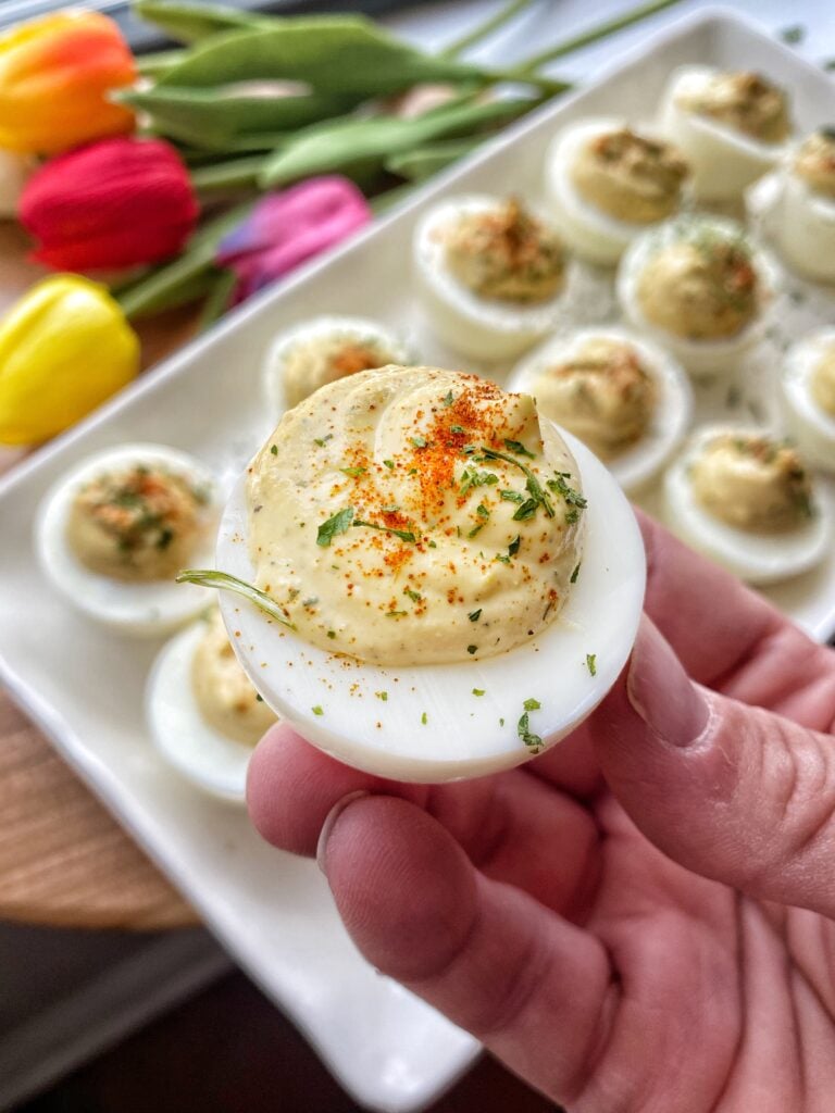 A simple deviled egg held above a plate of more of the eggs
