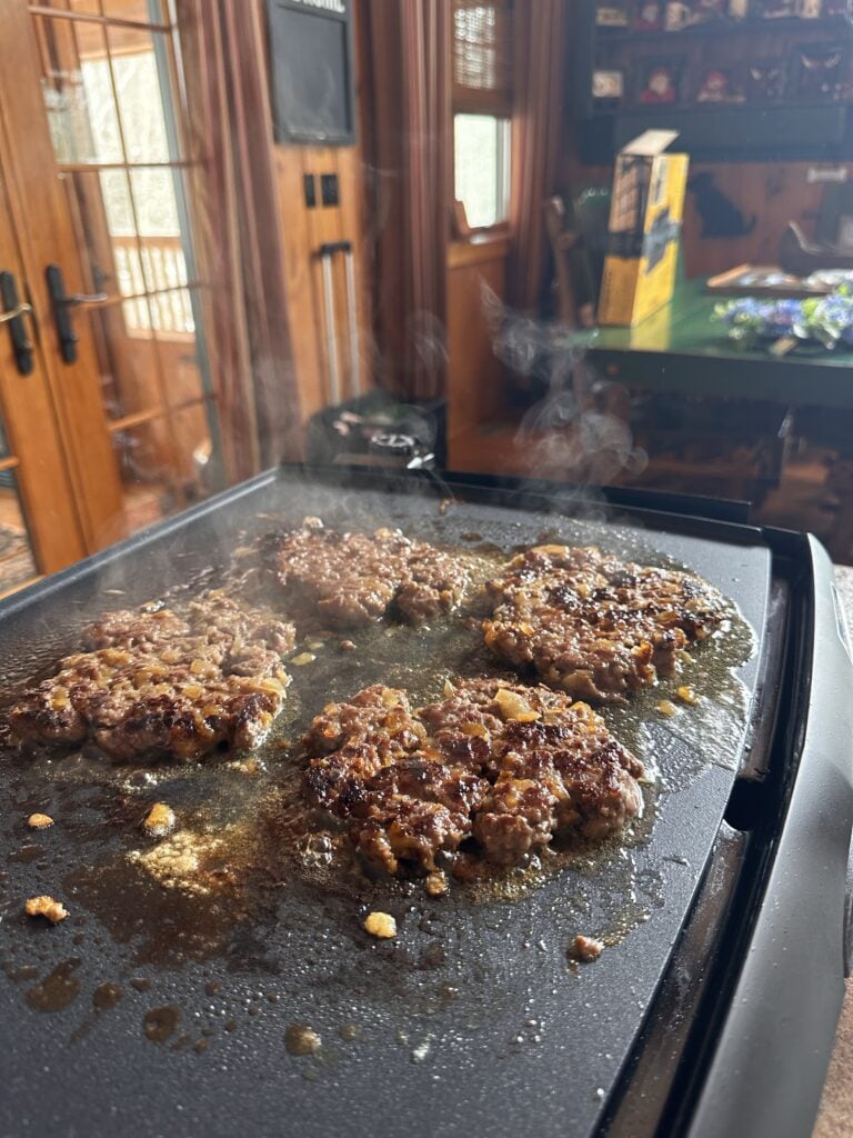 Four burger patties sizzling on the griddle