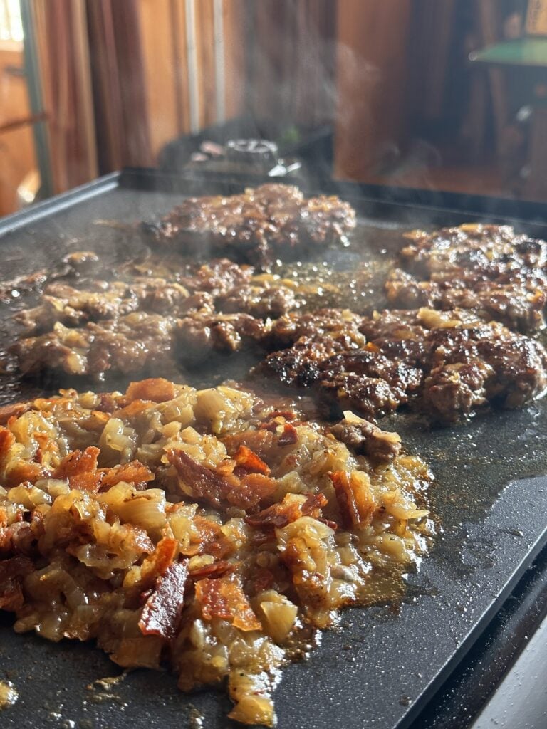A close up of burgers sizzling on the griddle