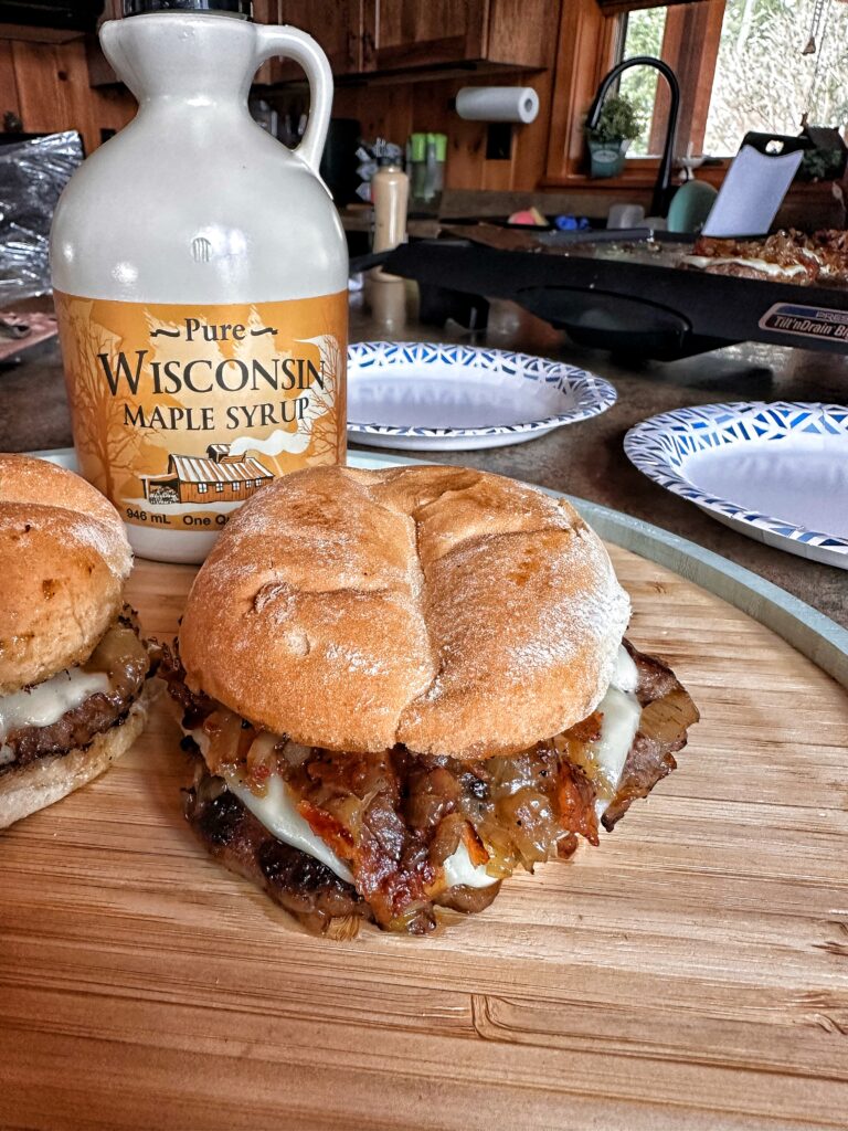 A Maple Bacon smash burger in front of a bottle of pure Wisconsin Maple Syrup