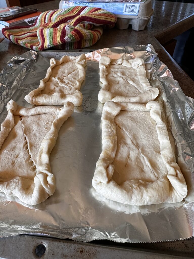 Crescent roll dough shaped into pastry form on a foil covered baking sheet