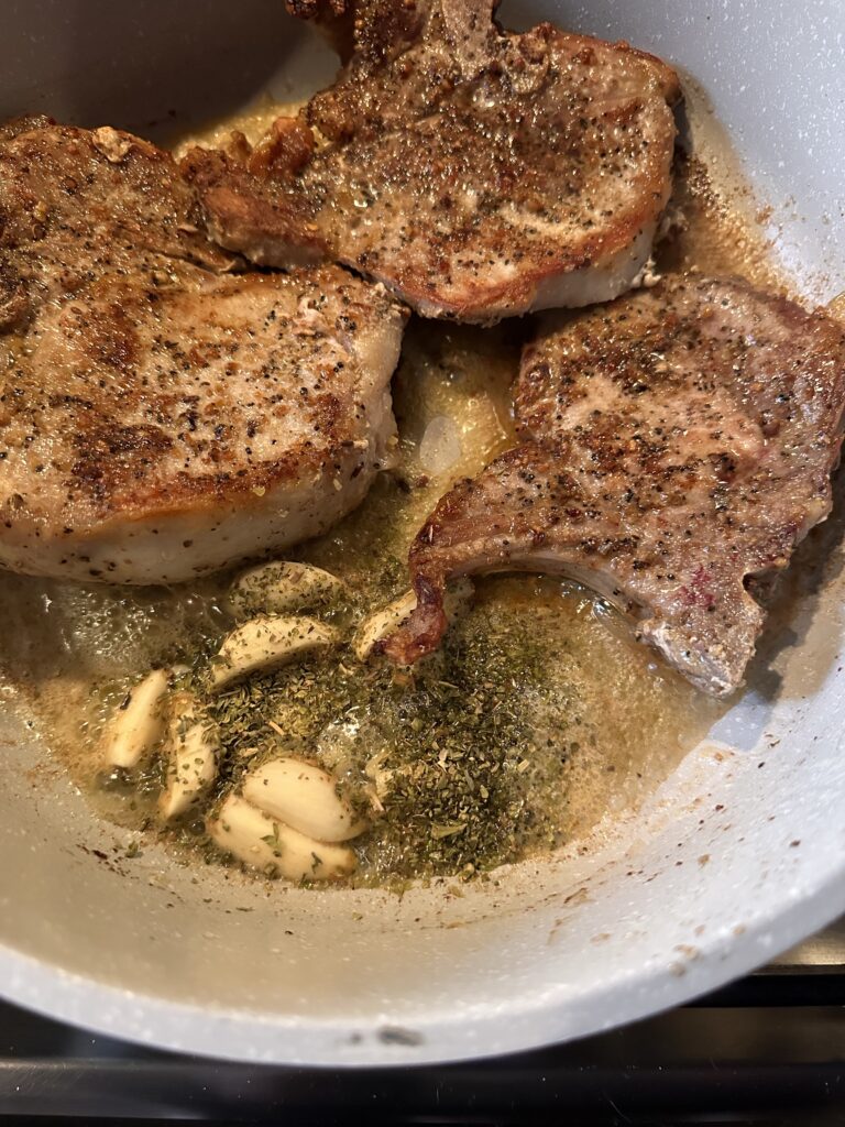 Pork chops cooking in a pan with garlic and spices