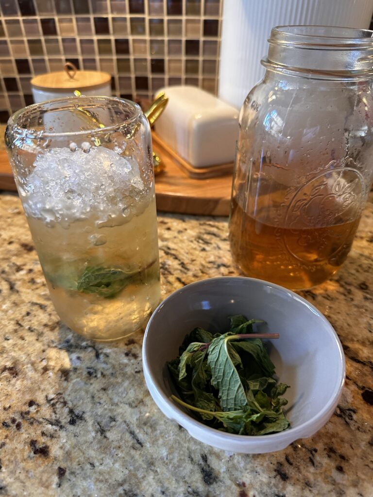 A glass of Derby Day Tea next to mint leaves